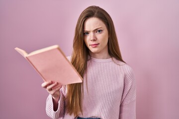 Young caucasian woman reading a book over pink background skeptic and nervous, frowning upset...