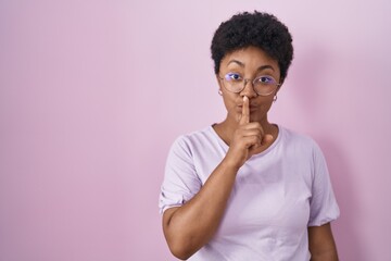 Fototapeta na wymiar Young african american woman standing over pink background asking to be quiet with finger on lips. silence and secret concept.