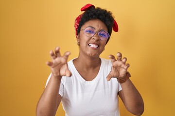 Young african american woman standing over yellow background smiling funny doing claw gesture as...