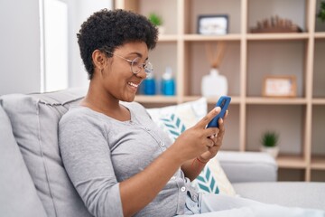 African american woman using smartphone sitting on sofa at home