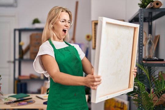 Young caucasian woman looking at canvas angry and mad screaming frustrated and furious, shouting with anger. rage and aggressive concept.