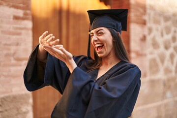 Young hispanic woman wearing graduated uniform doing spend money gesture with hands at university