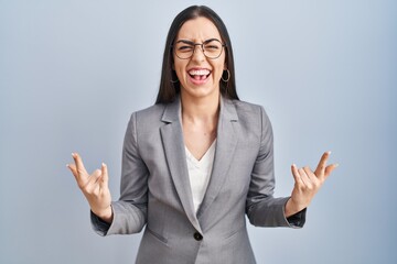 Hispanic business woman wearing glasses shouting with crazy expression doing rock symbol with hands up. music star. heavy concept.