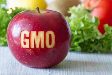 GMO text on red apple, vegetables and fruits in background, concept of genetically modified foods