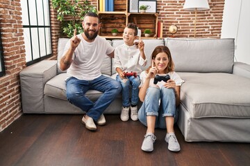 Family of three playing video game sitting on the sofa surprised with an idea or question pointing...