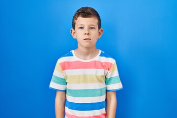 Young caucasian kid standing over blue background relaxed with serious expression on face. simple and natural looking at the camera.