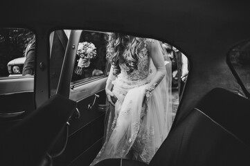 Happy bride and groom, newlywed wedding couple is sit in a retro car on a country road for honeymoon after the ceremony. The best day and marriage. Just married. Black and white photo.