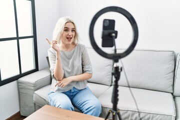 Fototapeta na wymiar Young caucasian woman recording vlog tutorial with smartphone at home with a big smile on face, pointing with hand and finger to the side looking at the camera.