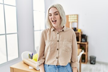 Young beautiful caucasian woman at construction office winking looking at the camera with sexy expression, cheerful and happy face.