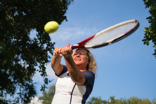 Mature Woman Playing Tennis Serving A Ball Outside.