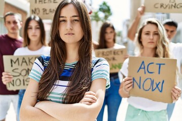 Young activist woman with arms crossed gesture standing with a group of protesters holding banner protesting at the city.