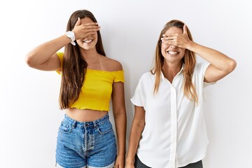 Mother and daughter together standing together over isolated background smiling and laughing with hand on face covering eyes for surprise. blind concept.