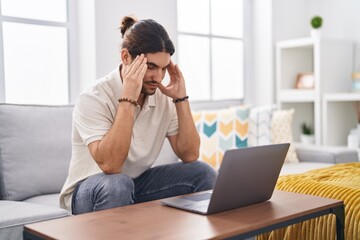 Young hispanic man stressed using laptop sitting on sofa at home