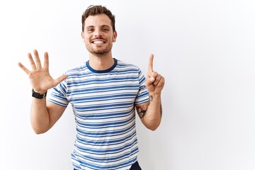 Handsome young man standing over isolated background showing and pointing up with fingers number six while smiling confident and happy.