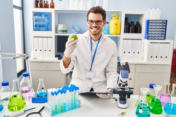 Young hispanic man scientist holding apple at laboratory