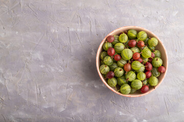 Fresh red and green gooseberry in ceramic bowl on gray concrete, top view, copy space.