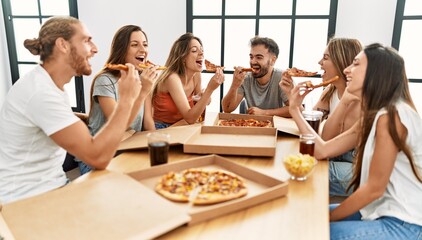 Group of young people smiling happy eating italian pizza sitting on the table at home