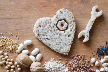 Whole grains products, groats, nuts, legumes, seeds on wooden background. Wrench, screw and heart made of bread, healthy heart diet concept abstract