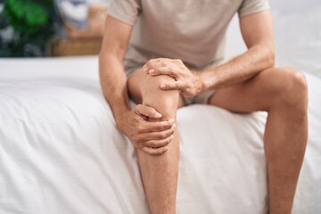 Young man suffering for knee injury sitting on bed at bedroom