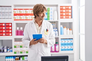 Young man pharmacist smiling confident using touchpad at pharmacy