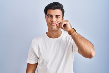 Fototapeta premium Hispanic man standing over blue background mouth and lips shut as zip with fingers. secret and silent, taboo talking