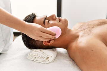 Fototapeta na wymiar Young hispanic man relaxed having facial treatment cleaning face electric cleaner at beauty center
