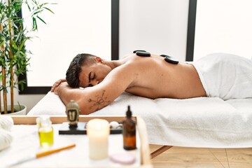 Obraz na płótnie Canvas Young hispanic man relaxed having back massage using black stones at beauty center