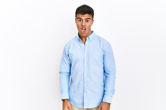 Young hispanic man wearing business shirt standing over isolated background in shock face, looking skeptical and sarcastic, surprised with open mouth