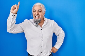 Middle age man with grey hair standing over blue background pointing finger up with successful idea. exited and happy. number one.