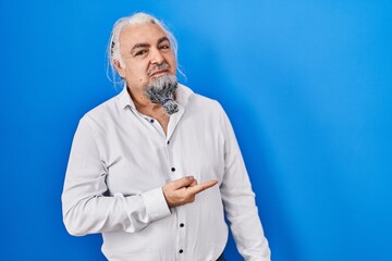Middle age man with grey hair standing over blue background pointing aside worried and nervous with...