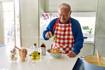 Senior man smiling confident pouring oregano on spaghetti at kitchen