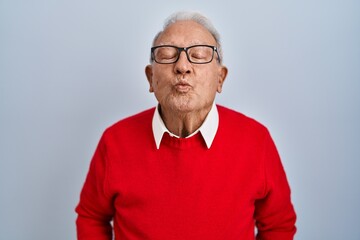 Senior man with grey hair standing over isolated background looking at the camera blowing a kiss on air being lovely and sexy. love expression.