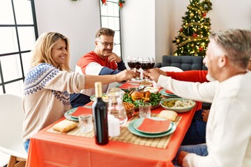 Group of middle age people smiling happy having christmas dinner toasting with wine at home.
