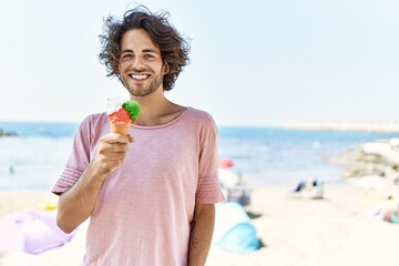 Young hispanic man smiling happy eating ice cream at the beach.