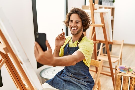 Young hispanic artist man drawing having video call using smartphone at art studio.