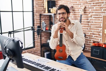 Young hispanic man musician holding ukulele at music studio