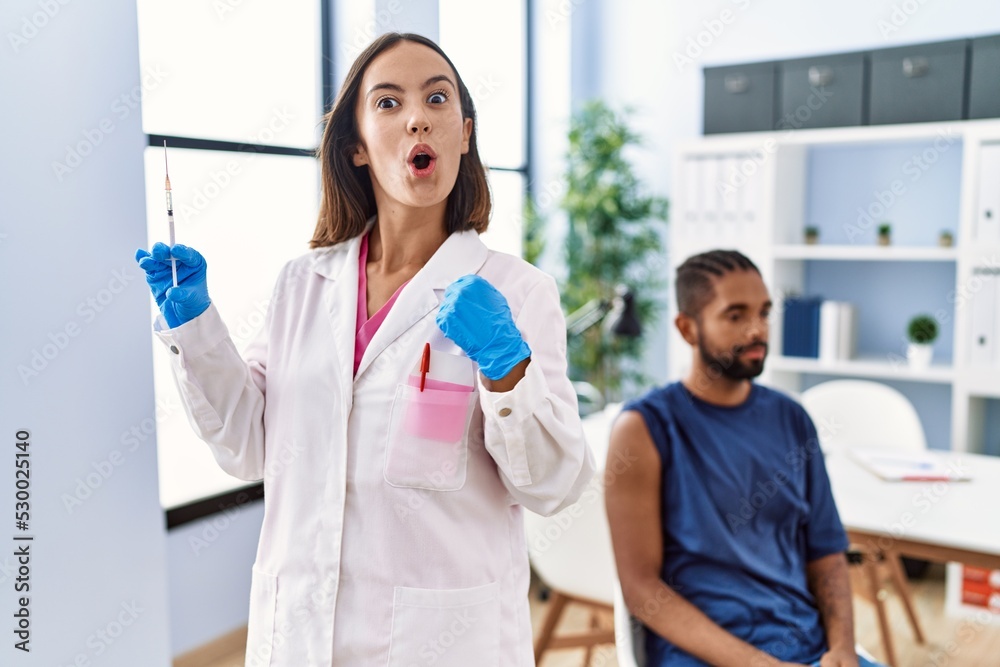 Canvas Prints young doctor woman holding vaccine showing syringe scared and amazed with open mouth for surprise, d