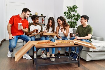 Group of young friends smiling happy eating italian pizza sitting on the sofa at home.