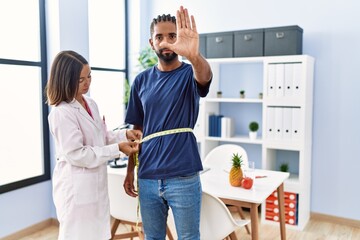 Dietitian at the clinic using tape measure measuring waist of client with open hand doing stop sign...