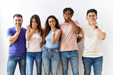 Obraz premium Group of young people standing together over isolated background laughing and embarrassed giggle covering mouth with hands, gossip and scandal concept