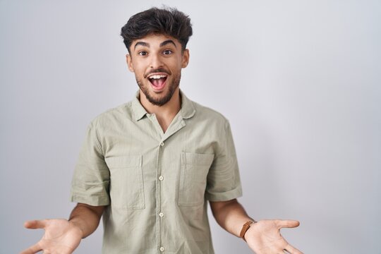 Arab man with beard standing over white background smiling cheerful with open arms as friendly welcome, positive and confident greetings