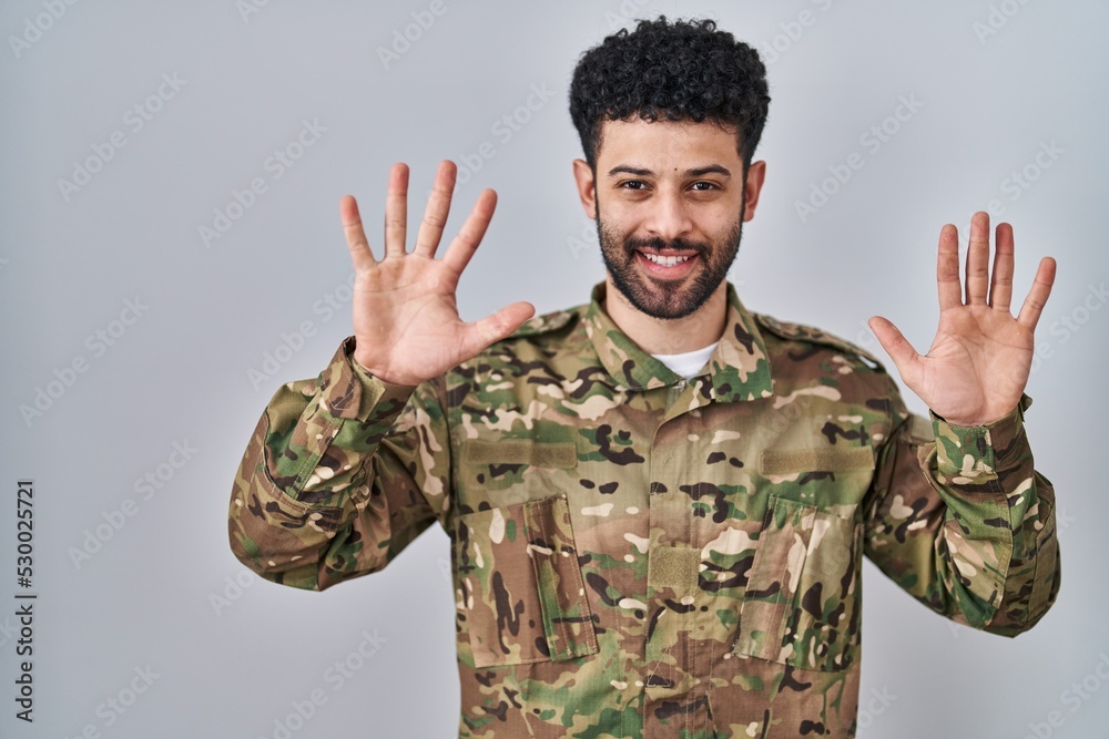 Poster arab man wearing camouflage army uniform showing and pointing up with fingers number ten while smili