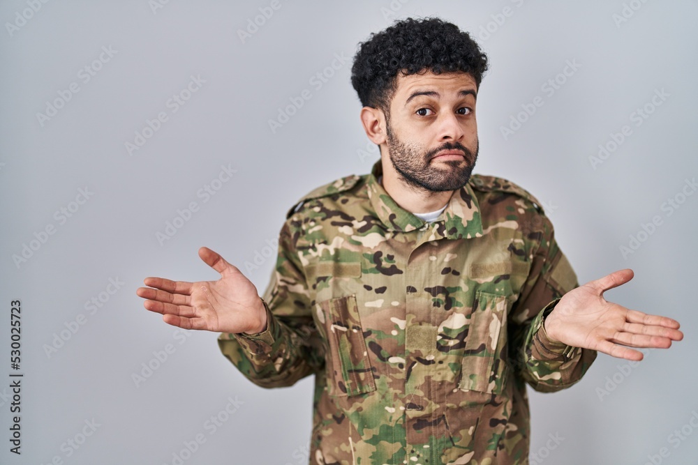 Poster arab man wearing camouflage army uniform clueless and confused expression with arms and hands raised