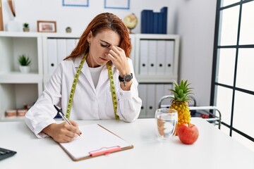 Young redhead woman nutritionist doctor at the clinic tired rubbing nose and eyes feeling fatigue...