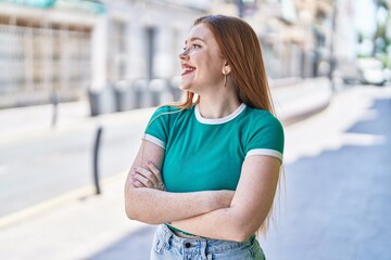 Young redhead woman standing with arms crossed gesture at street