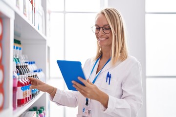 Young blonde woman pharmacist using touchpad working at pharmacy