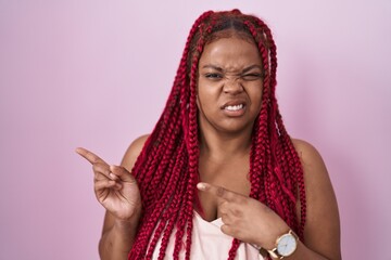 African american woman with braided hair standing over pink background pointing aside worried and...