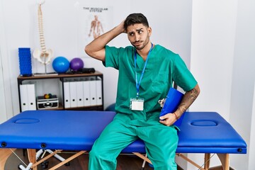 Young physiotherapist man working at pain recovery clinic confuse and wondering about question....