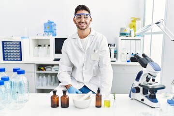 Young hispanic man working at scientist laboratory looking positive and happy standing and smiling...