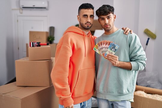 Young Hispanic Gay Couple Moving To A New Home Holding Banknotes Thinking Attitude And Sober Expression Looking Self Confident